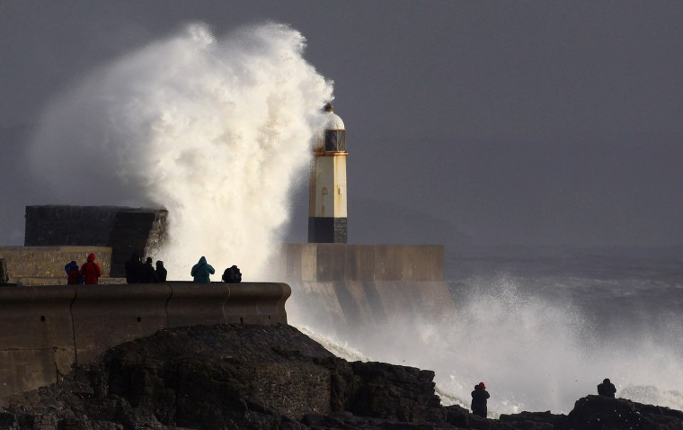 People take photographs of waves crashing against the harbor wall on Jan. 3, 2012 in Porthcawl, Wales. High winds gusting up to 95mph and heavy rain have been affecting many parts of the country disrupting travel and causing damage to buildings.
