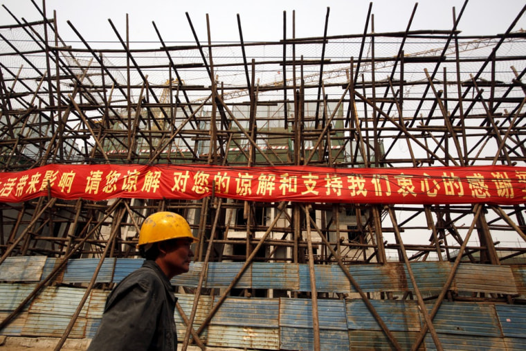 A construction worker walks past a banner at a building site for new apartment blocks located on the outskirts of Beijing.