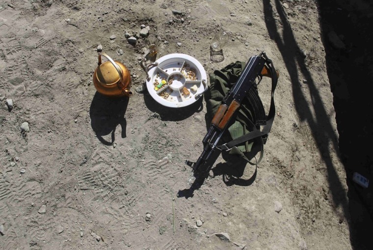 An AK-47 rifle belonging to an Afghan policeman lies on the ground as other policemen grill meat during the celebration of the Muslim Eid Al Adha festival in COP Sar Howza in Paktika province on October 26, 2012.