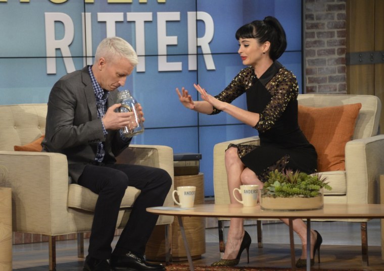 Anderson Cooper takes a sniff of Krysten Ritter's jar of wolf urine.