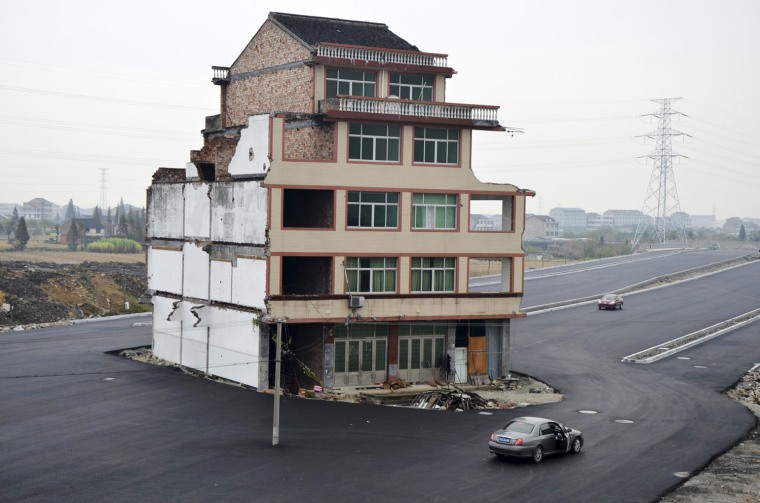 A car stops beside a house in the middle of a newly built road in Wenling, China, on Thursday. Two couples have refused to agree to allow their homes to be demolished.