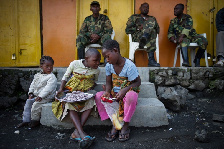 Congolese children sit on a step in front of M23 rebels in Sake, Nov. 22, 2012. Rebels took the town yesterday, but were engaged in heavy gunfighting this afternoon as government-allied militia tried to retake it.