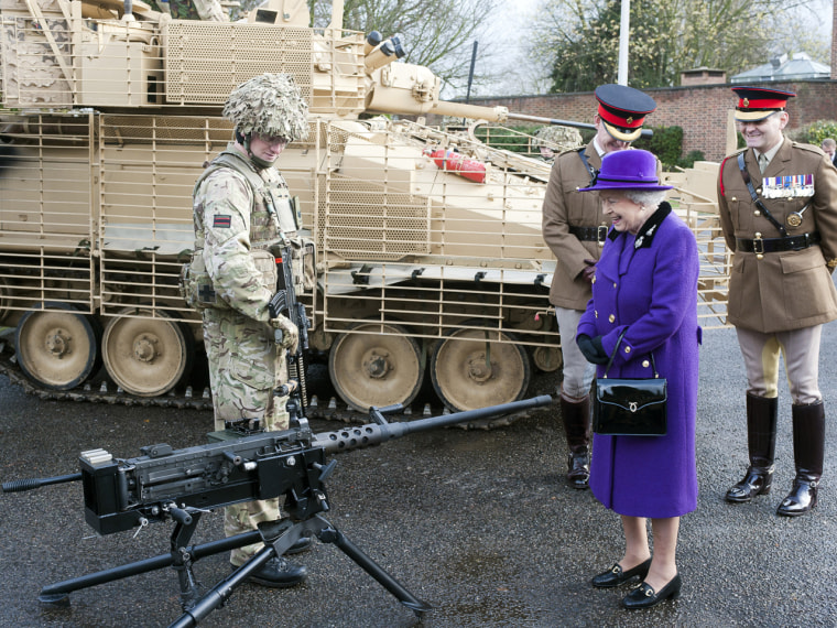 The Queen laughs while looking at a machine gun with members of the Household Cavalry.