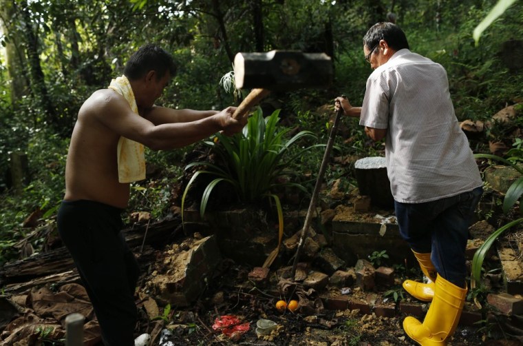 Mr Sim, left, breaks a tombstone with his sledgehammer as he exhumes a grave at Bukit Brown cemetery with his boss, Mr Leung.