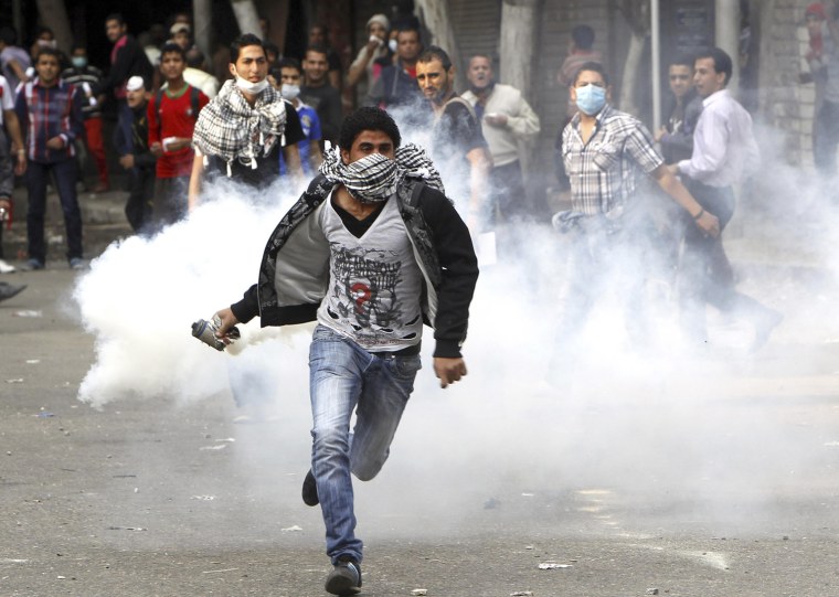 A protester runs to throw a tear gas canister back to riot police during clashes in Cairo's Tahrir Square on Tuesday. President Mohammed Morsi's declaration last week of new powers for himself has sparked days of demonstrations.