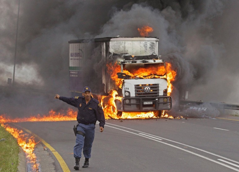 A police officer reacts as flames and smoke emerge from a truck after it was set alight by striking truck drivers, on a slipway off a main highway leading out of the city of Cape Town, South Africa, Oct. 3. South African truck workers have been on strike for the past two week with sporadic violence reported.