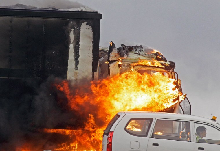 A car drives by a truck on fire on a slipway off a main highway leading out of the city of Cape Town, South Africa, Oct. 3.