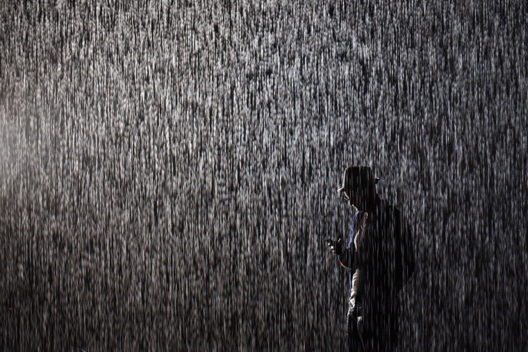 A man checks his phone as he experiences the 'Rain Room' art installation by 'Random International' in The Curve at the Barbican Centre on Oct. 3, in London, England.