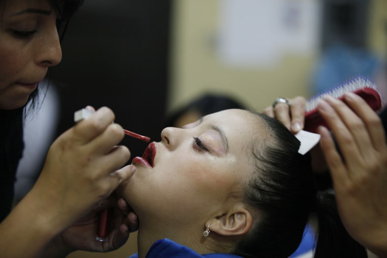 A cast member holds still as her make-up is applied and hair is brushed in preparation for her performance in