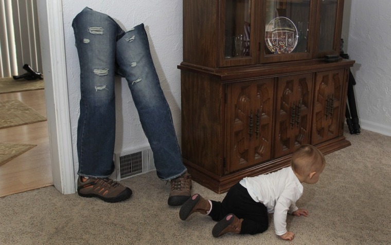 Chloe Mills, 1-year-old daughter of Army Staff Sgt. Travis Mills and his wife Kelsey, crawls past her father's walking legs in his boyhood home in Vassar, Mich., on Oct. 4, 2012.