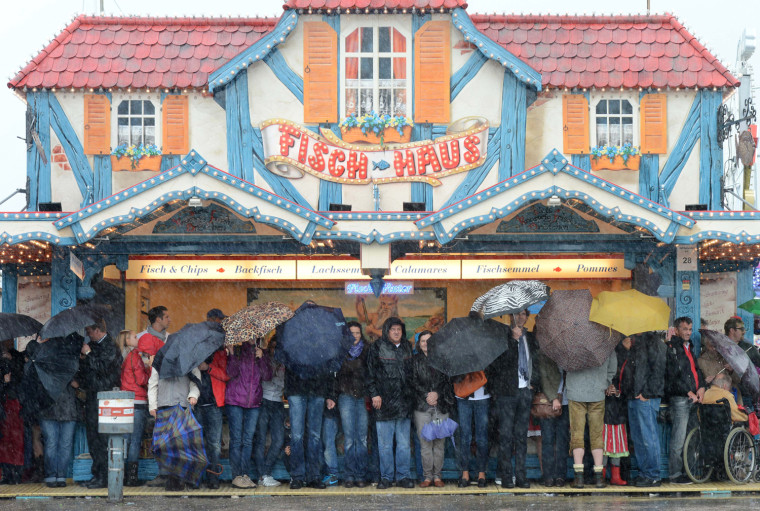 Visitors of the Oktoberfest festival wait during the rain in front of a booth at Oktoberfest festival fair ground at the Theresienwiese in Munich, southern Germany, on Oct. 7, the last day of the world famous beer festival.