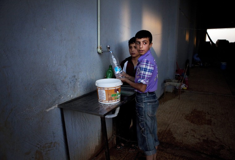 Syrian refugee boys fill bottles with water in an abandoned storage house which is part of a camp at the Syrian-Turkish border near Azaz, Syria, Oct. 7.