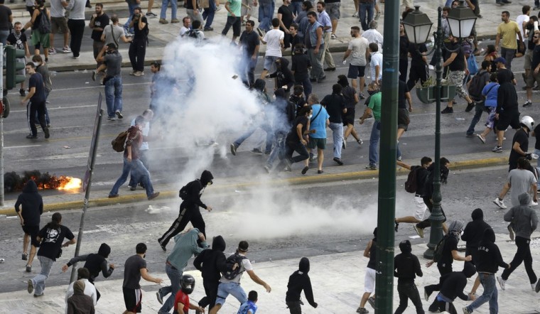 Protestors run away from tear gas during clashes in front of the parliament in Athens on Tuesday Oct. 9, 2012.