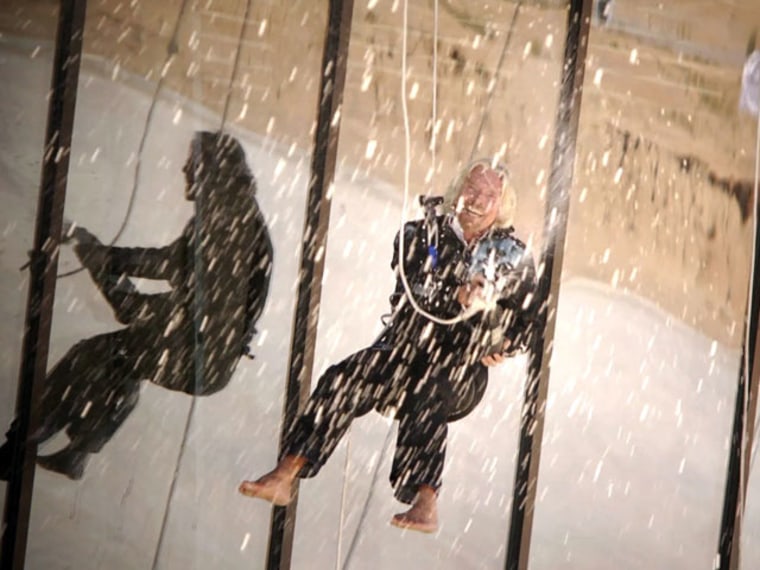 Virgin Galactic founder Richard Branson sprays champagne from a bottle as he hangs from a rope along the side of Spaceport America's nearly completed terminal/hangar facility in New Mexico.