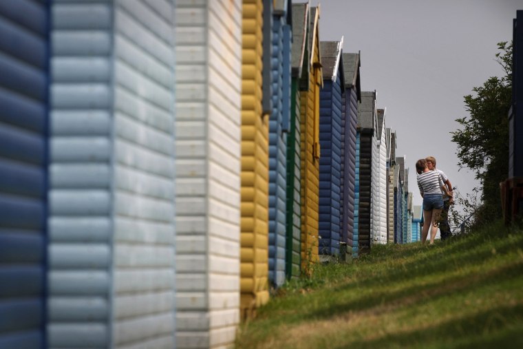 A young couple kiss behind a row of beach huts on Wednesday, Aug. 3, in Whitstable, England.