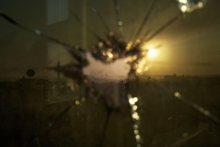 Smoke rises from buildings due to shelling by government forces, seen through broken glass in Aleppo on October 13, 2012.