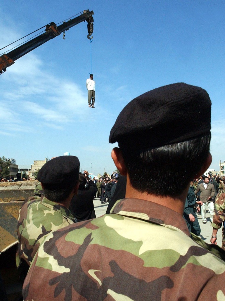 Two Iranian police officers look at the dangling body of Mohammed Bijeh, convicted of raping and murdering 16 children, after he was hanged from a construction crane in a public execution in Pakdasht, Iran, on March 16, 2005.