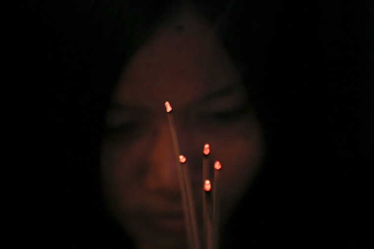 A young woman holds incense sticks while praying.