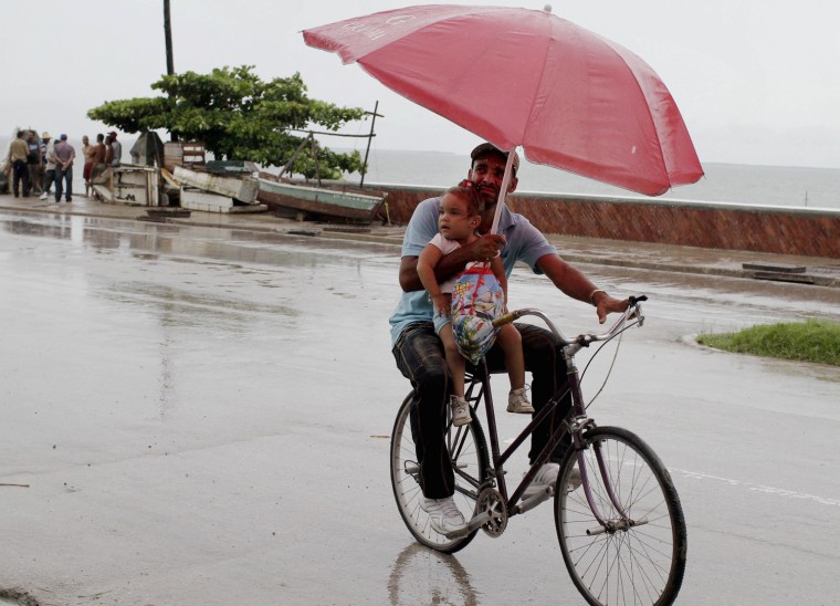 A man balances a child and umbrella on his bike as it rains during the approach of Hurricane Sandy in Manzanillo, Cuba, Oct. 24, 2012.
