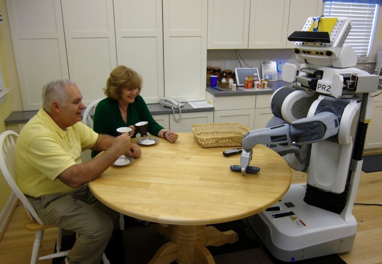 An elderly couple sits at table with their robot assistant.