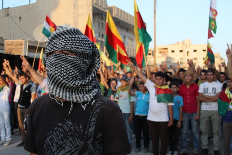 A new member of the Kurds' Popular Protection Units (YPG) stands in front of a crowd waving Kurdish flags in Qamishli, Syria. The Kurds are the largest ethnic group in the world without a homeland, totaling more than 30 million people.
