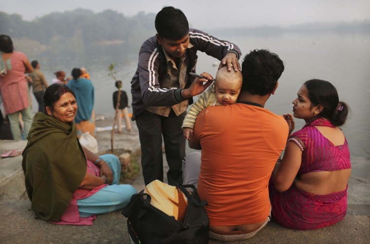 A barber gives Hindu boy Vanshu, 5 months, his first haircut as he is held by father Amit, second right, as his mother Rakhi Bansal, right, looks on before a holy dip in the Yamuna River on Oct. 29, 2012.