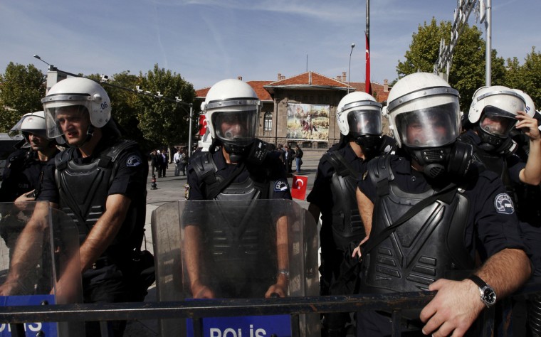 Police officers in riot gear stand watch as thousands of people prepare to march from the First National Assembly, seen in background, to the mausoleum of Ataturk to celebrate the Republic Day in Ankara, Turkey, Oct. 29.