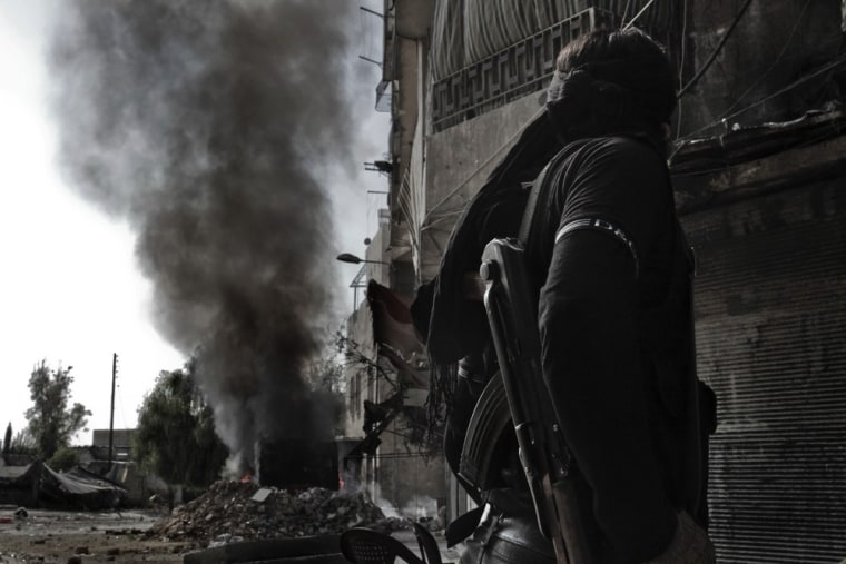 A rebel fighter looks at smoke billowing from a bus that caught on fire after a regime sniper allegedly shot at it in Aleppo on Oct. 28, 2012.