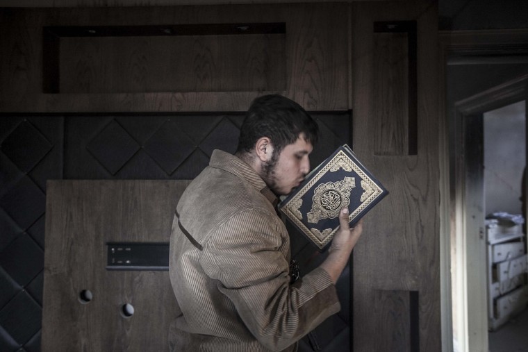 A rebel fighter belonging to the Liwa Al-Tawhid group kisses a Quran as mortar explosions and gunshots are heard in the nearby battlefield in the Karm al-Jabel neighborhood of Aleppo on Oct. 28, 2012.