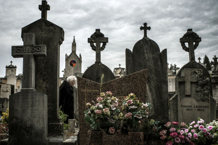 A woman stands in front of a tombstone in a cemetery in Lyon on the eve of All Saints' Day.