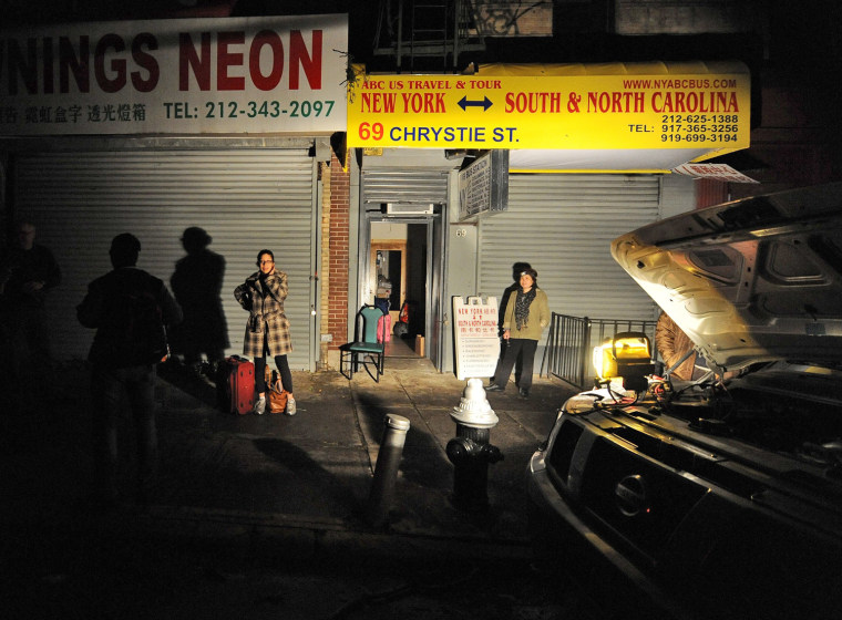 People are illuminated by a light from a car battery as they wait to leave the city on a bus heading to North Carolina from the Chinatown area of New York on Oct. 30.