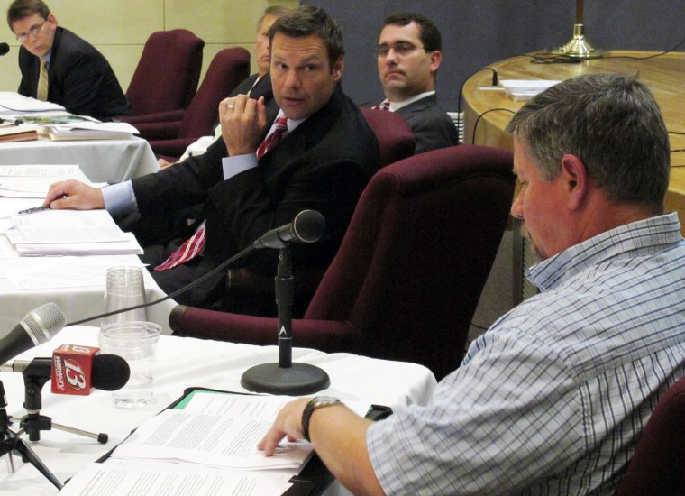 Kansas Secretary of State Kris Kobach, center, questions Joe Montgomery, lower right, a Manhattan, Kan., resident, during a meeting of the State Objections Board, Thursday, Sept. 13, 2012, in Topeka, Kan. The board includes Kobach and, behind him, Attorney General Derek Schmidt and is reviewing Montgomery's objection to the state listing President Barack Obama on its November election ballot.