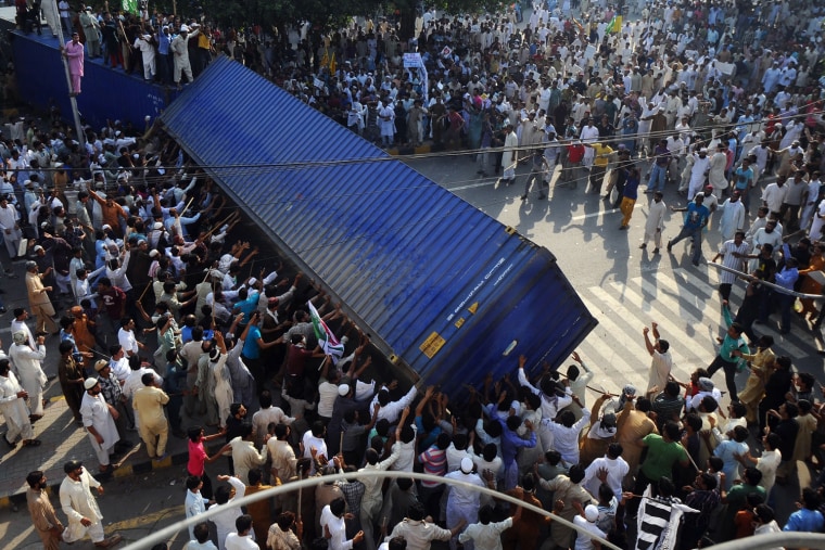 Pakistani Muslim demonstrators topple a freight container, placed by police to block a street during a protest against an anti-Islam film in Lahore on Sept. 21. At least 13 people died and nearly 200 were wounded in Pakistan during violent protests on Friday condemning a US-made film insulting Islam, defying a government call for only peaceful demonstrations, officials said.