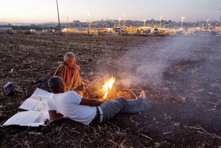 Palestinian workers warm themselves by a fire after crossing from the West Bank into Israel through the Zufim Checkpoint (behind), near Kochav Yair, Israel on September 27, 2012. They will be picked up by Israeli foremen for a day's labor inside Israel and are among the tens of thousands who have permits from Israel to cross from the West Bank and work inside Israel.