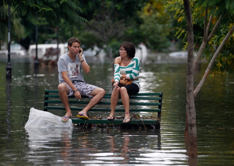 Residents sit on a bench in a flooded public square.