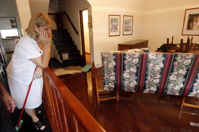 A woman looks at the flooded living room of her home.