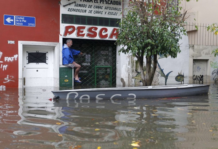 A man perches above the water next to a boat in a flooded street.