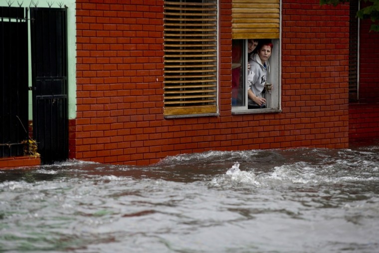 A couple looks at their flooded street from behind their home's window in La Plata, in Argentina's Buenos Aires province, Wednesday, April 3, 2013.
