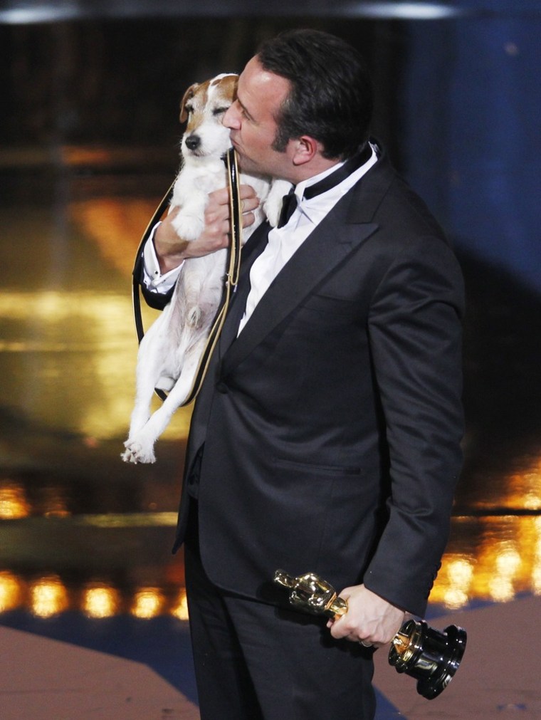 Best actor winner Jean Dujardin kisses Uggie the dog from \"The Artist\" after their film won best picture.