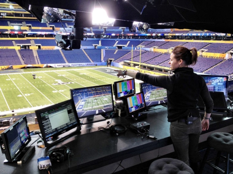 Jenna stands in front of Al Michael's seat in the NBC broadcast booth for the Super Bowl.