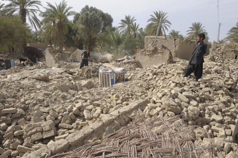 Pakistani earthquake survivors stand on the rubble of their collapsed mud houses in the Mashkel area of southwest Paskitan, Wednesday.