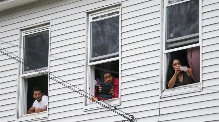 Onlookers take pictures as they watch from windows while SWAT team members search for one remaining suspect at a neighboring apartment building on April 19, in Watertown, Mass.