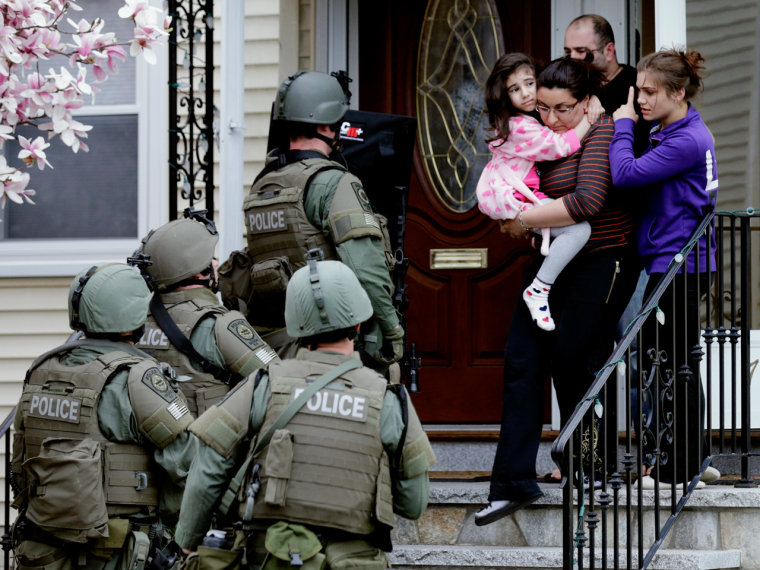 A woman carries a girl from their home as a SWAT team searching for a suspect in the Boston Marathon bombings enters the building in Watertown, Mass., Friday, That was part of what turned out to be a chaotic week in the U.S.