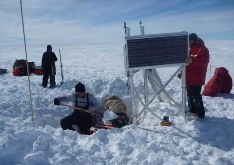 Researchers hard at work around a seismograph, an instrument in the orange box buried in a hole in the snow. Solar power runs the seismic station during the summer, and batteries keep it going during the long, dark winter months.