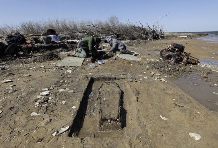 Archaeologist Joanna Wilson, left, and Thomas Klatka work on a grave site being claimed by the sea on the north end of Tangier Island, Va., on April 3. A child's coffin is unearthed in the foreground. Climate change is accelerating what experts say will be increasing flooding along the bay and the foreseeable demise of Tangier. Some areas of the island are losing up to 15 feet of land a year.
