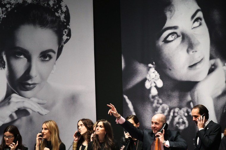 Auction house employees speak on the phone to bidders under pictures of Elizabeth Taylor at Christie's, where hundreds of items once belonging to the iconic actress went on the auction block in New York.