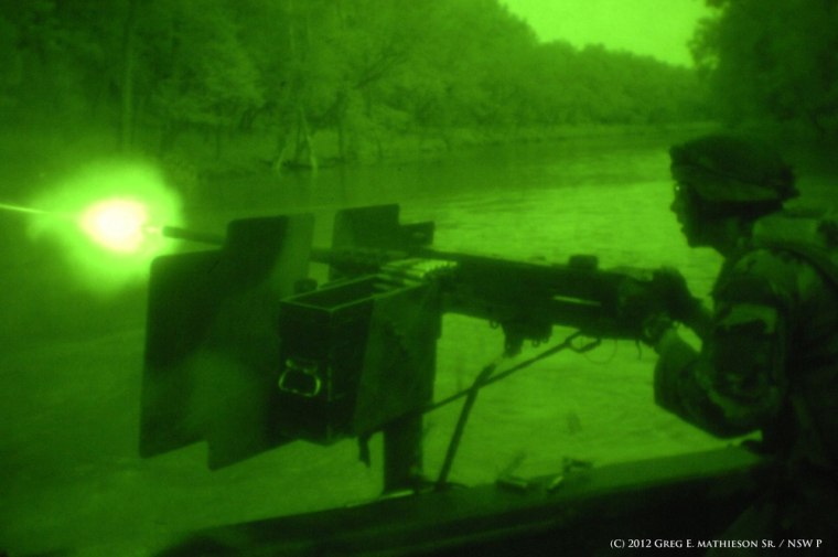 U.S. Naval Special Warfare Combatant-crew Crewman fires a 50 caliber machine gun from a Riverine boat in the darkness of night as seen through night vision goggles at a classified training location.