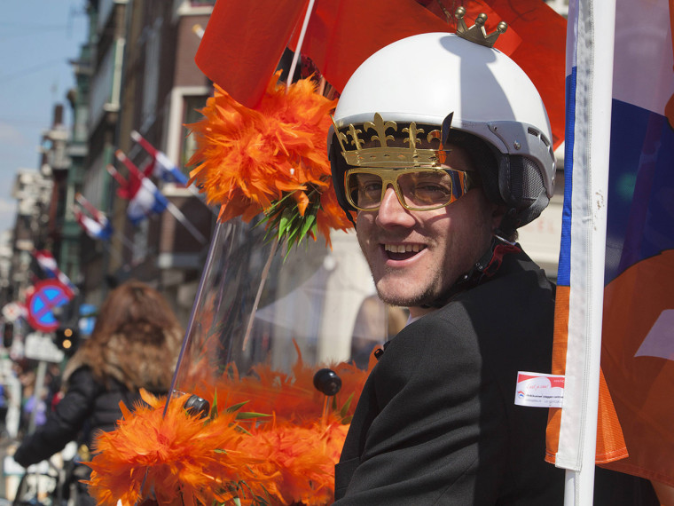 A man riding a scooter and wearing a crown on a helmet cruises the streets of Amsterdam April 28, 2013. The Netherlands is preparing for Queen's Day o...