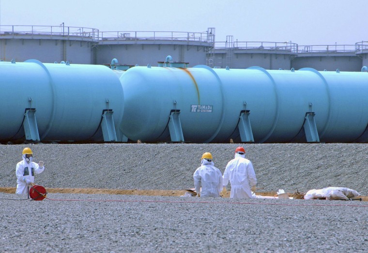 Workers stand among tanks used to store radioactive wastewater at the Fukushima Daiichi nuclear power plant on April 17.