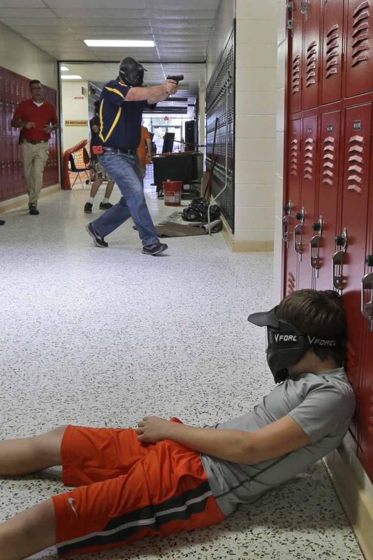 A Clarksville, Ark., schools faculty member, wearing a protective mask, carries a practice handgun toward a classroom in a training exercise July 11.